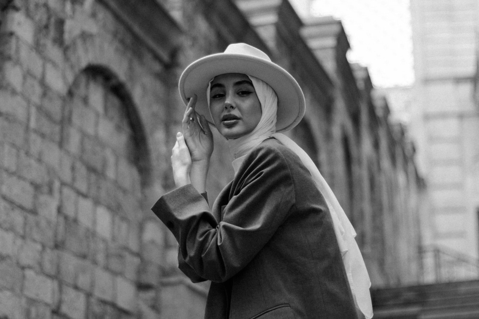 Black and white portrait of a young woman in a fedora and headscarf, exuding elegance and vintage charm.